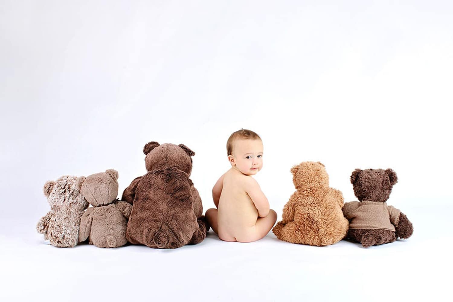 A baby looks back among stuffed teddy bears.