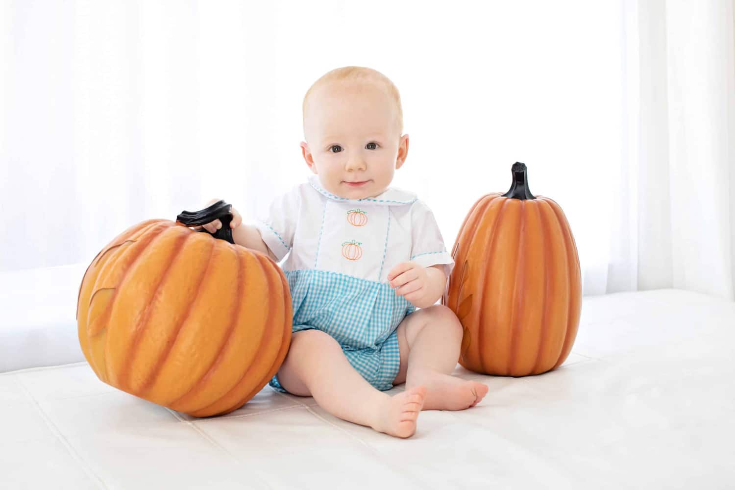 A baby takes a photo with two pumpkins.