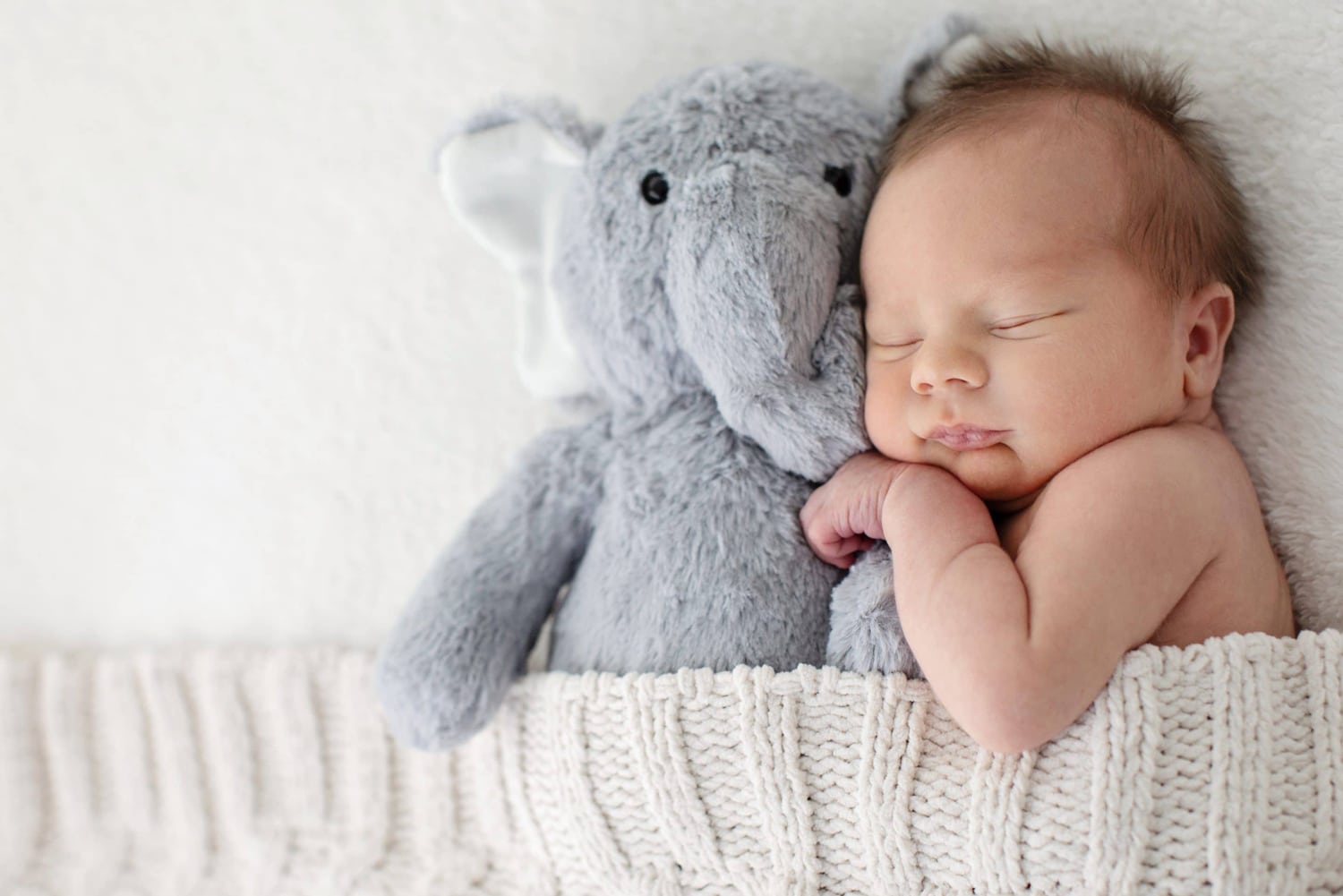 A baby clutches a gray stuffed elephant.