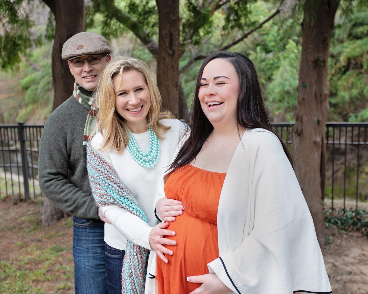 A surrogate mother in a red dress with the two parents.
