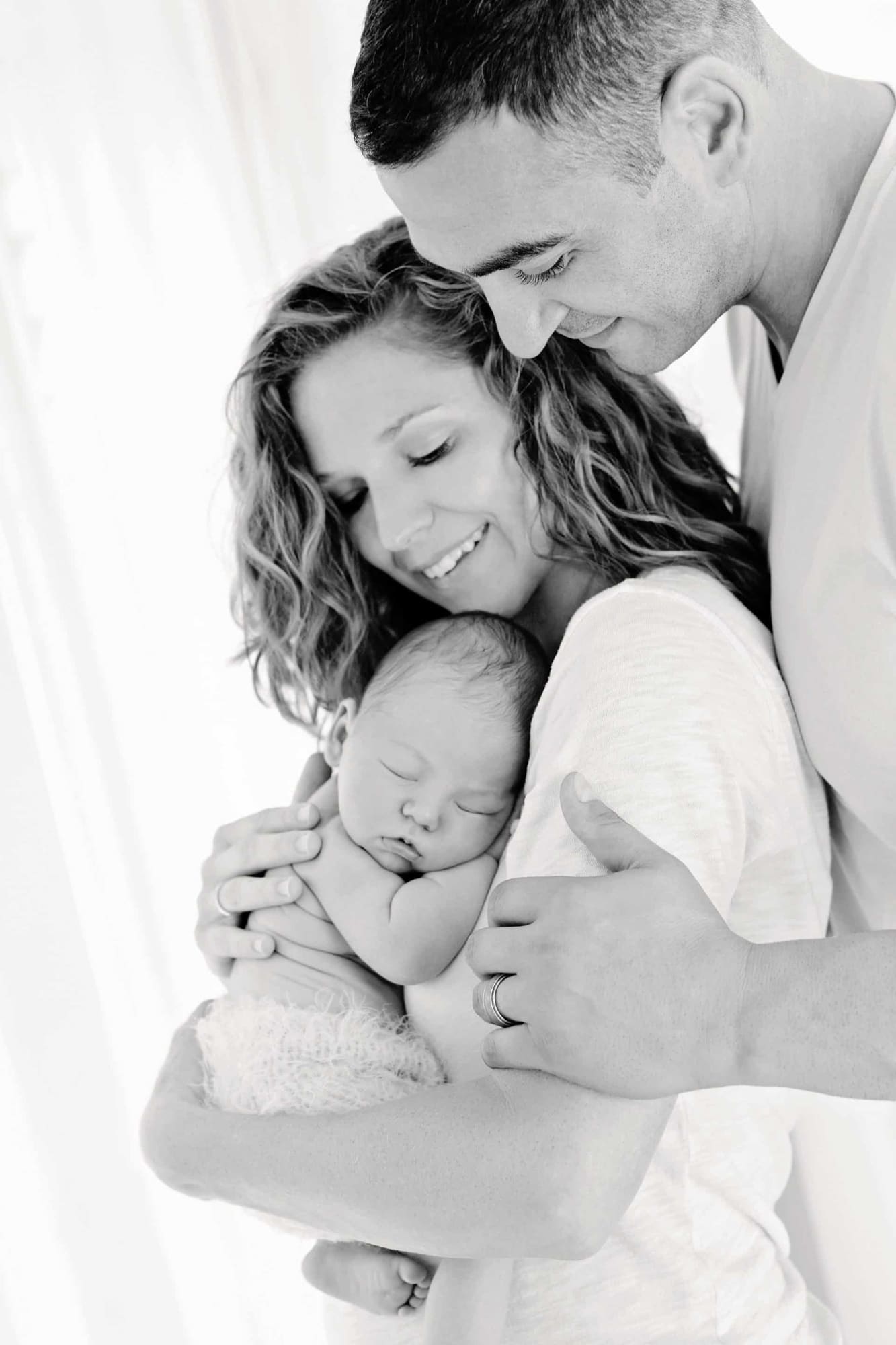 A smiling couple holds their newborn baby.