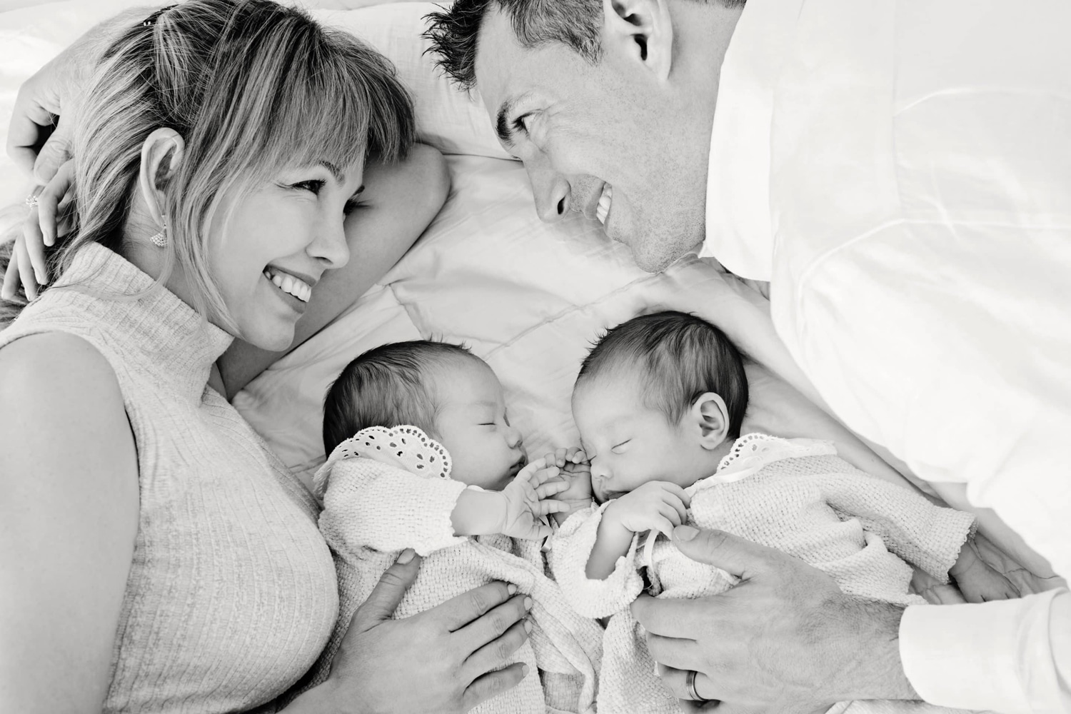 A husband and wife lay with their two newborn babies.