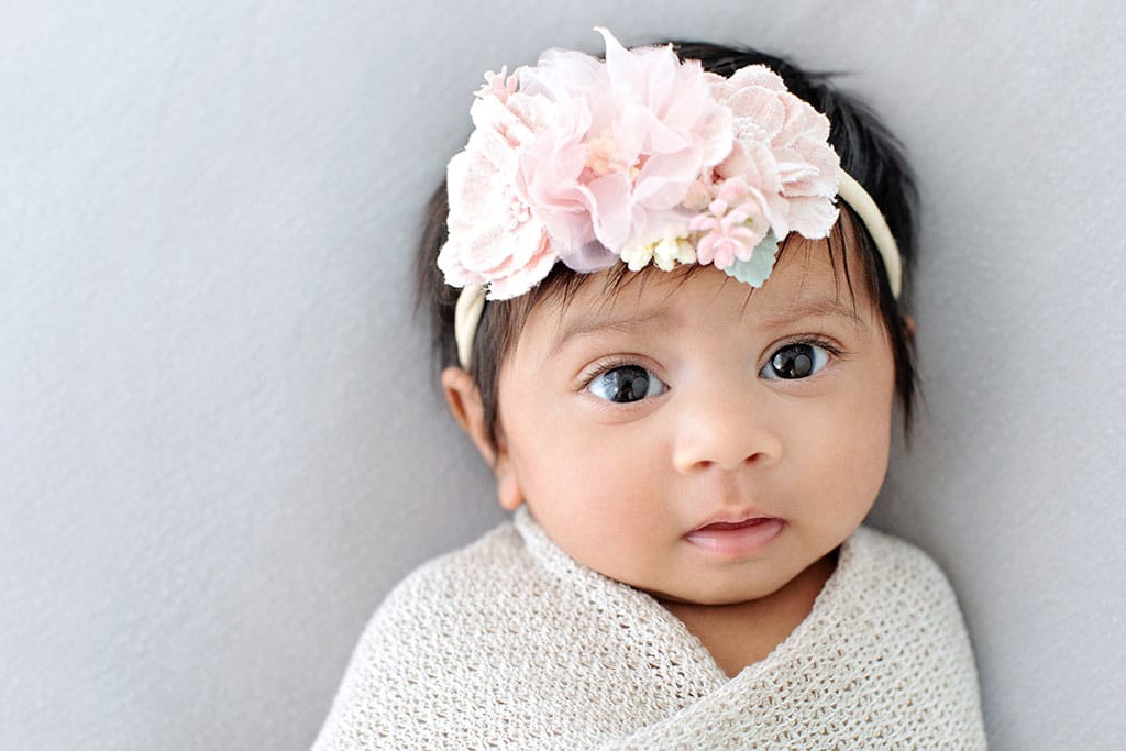 A three month old baby with a pink flower headband.