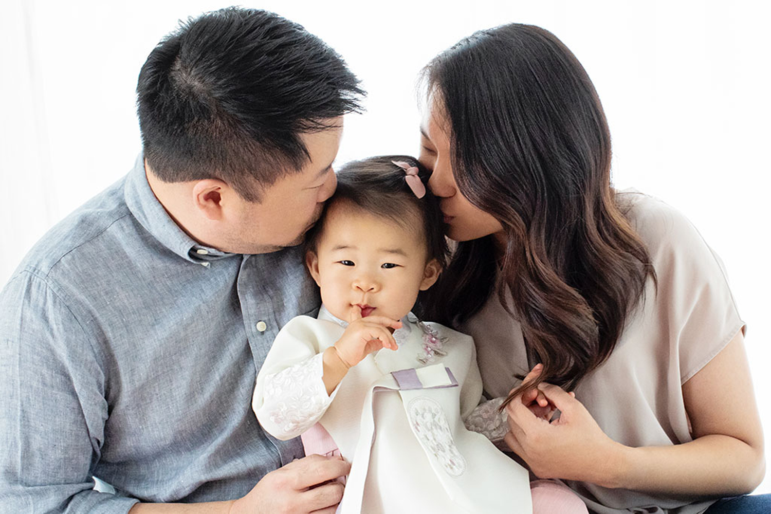 Two parents kiss their one-year-old.