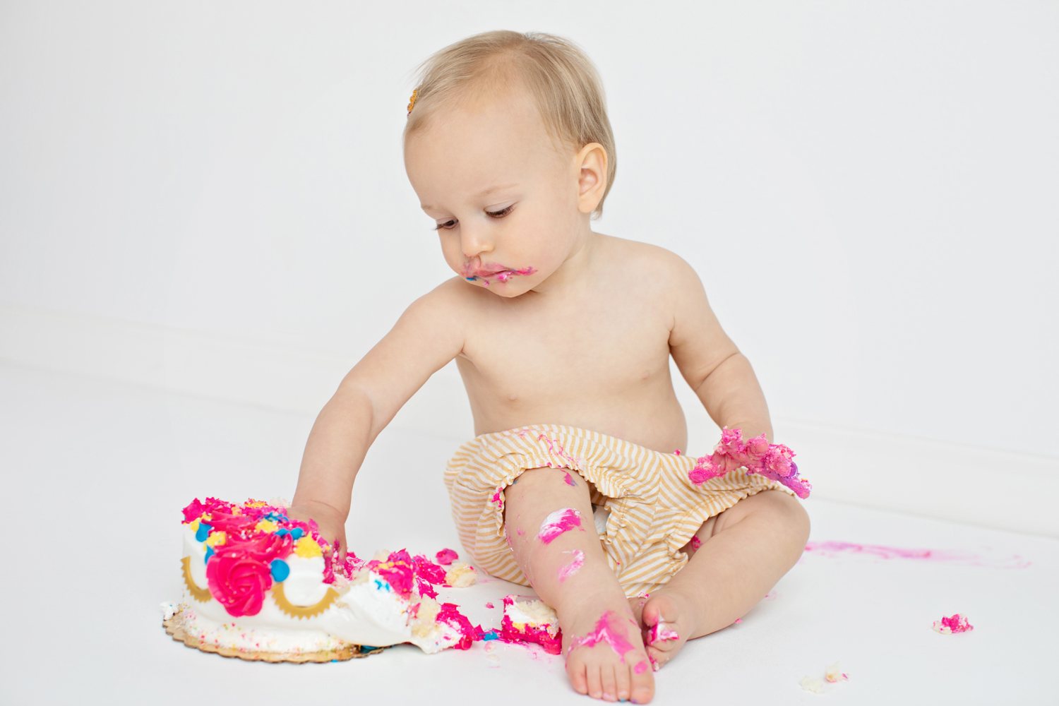 A one year old eats messy birthday cake.