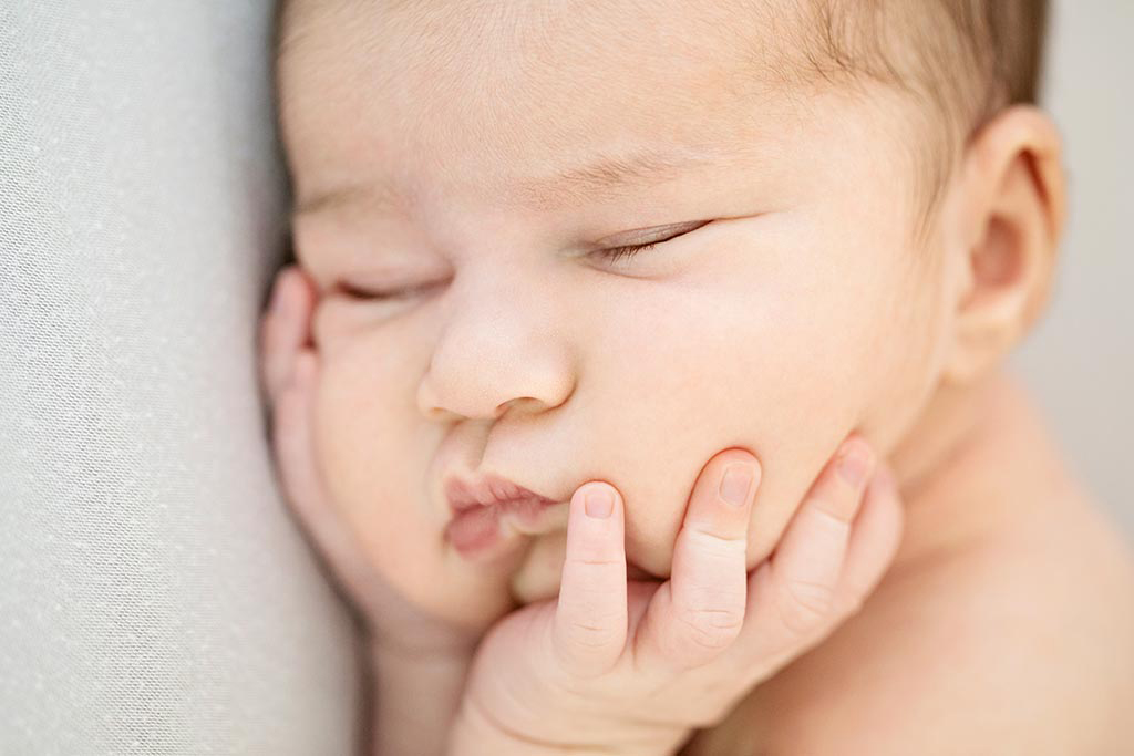 A newborn holds their face in their hands.