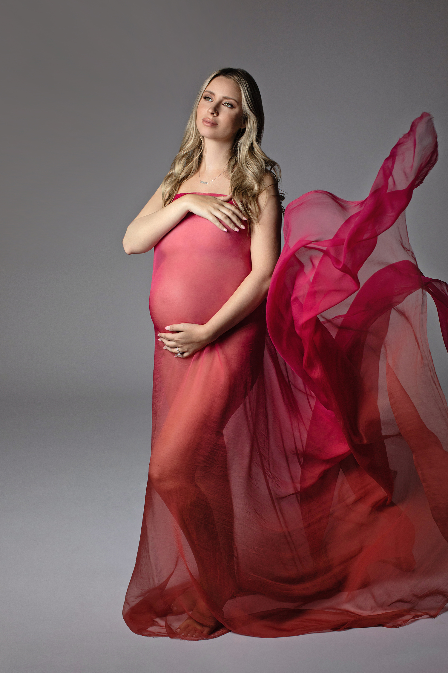 An alluring photograph of a glamorous mom-to-be, embraced by the soft fabrics of an exquisite gown, radiating luxury and grace in her maternity photoshoot.
