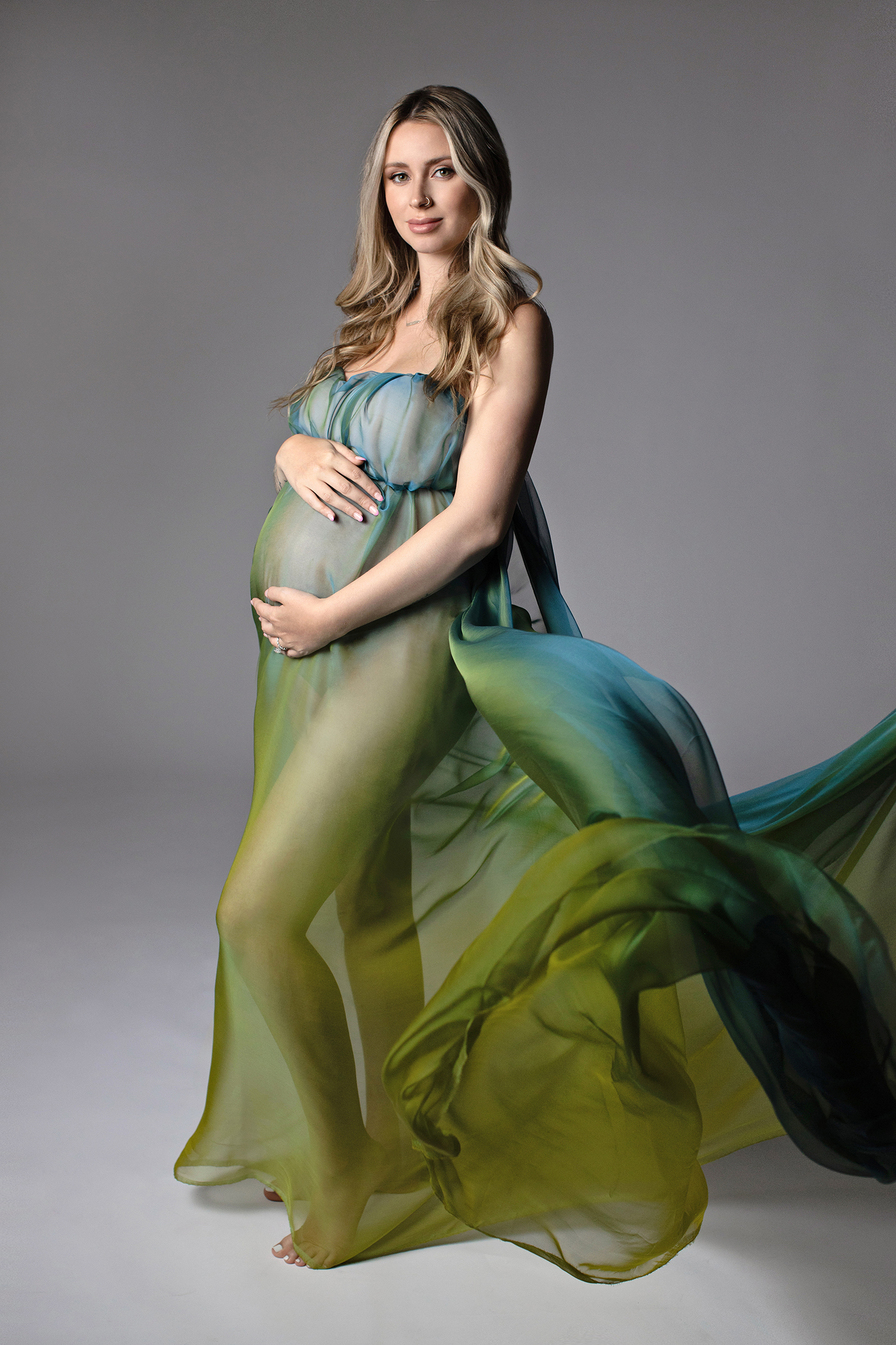 A photograph of a glamorous mom-to-be, embraced by the soft fabrics of an exquisite gown, radiating luxury and grace in her maternity photoshoot.