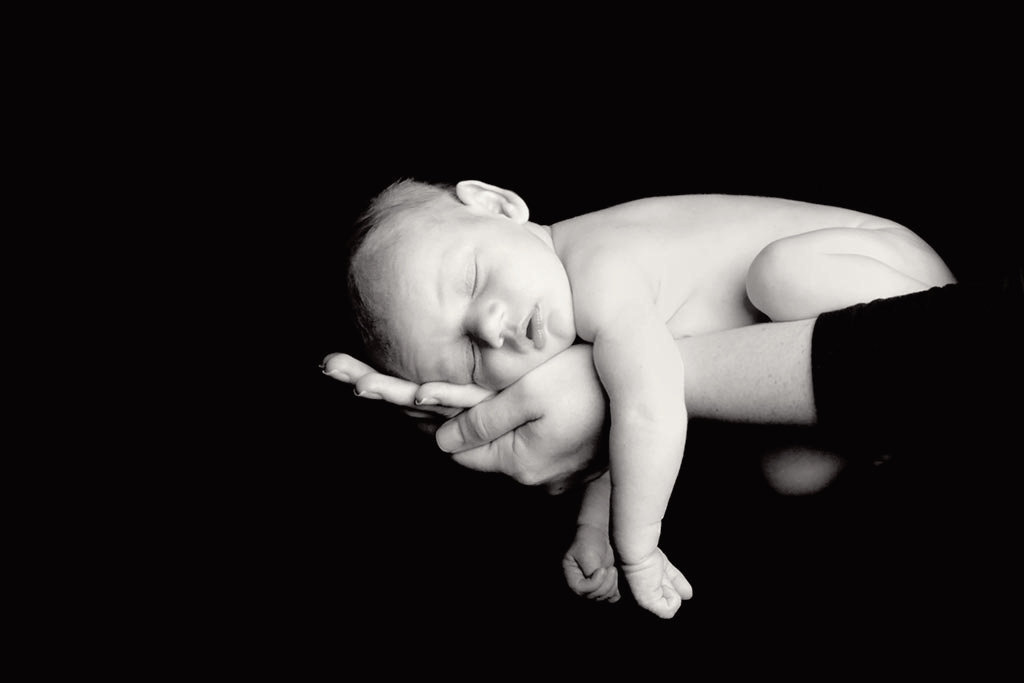 A black and white photograph showcasing the delicate features of a newborn baby, with wispy hair and closed eyes, radiating innocence and serenity.