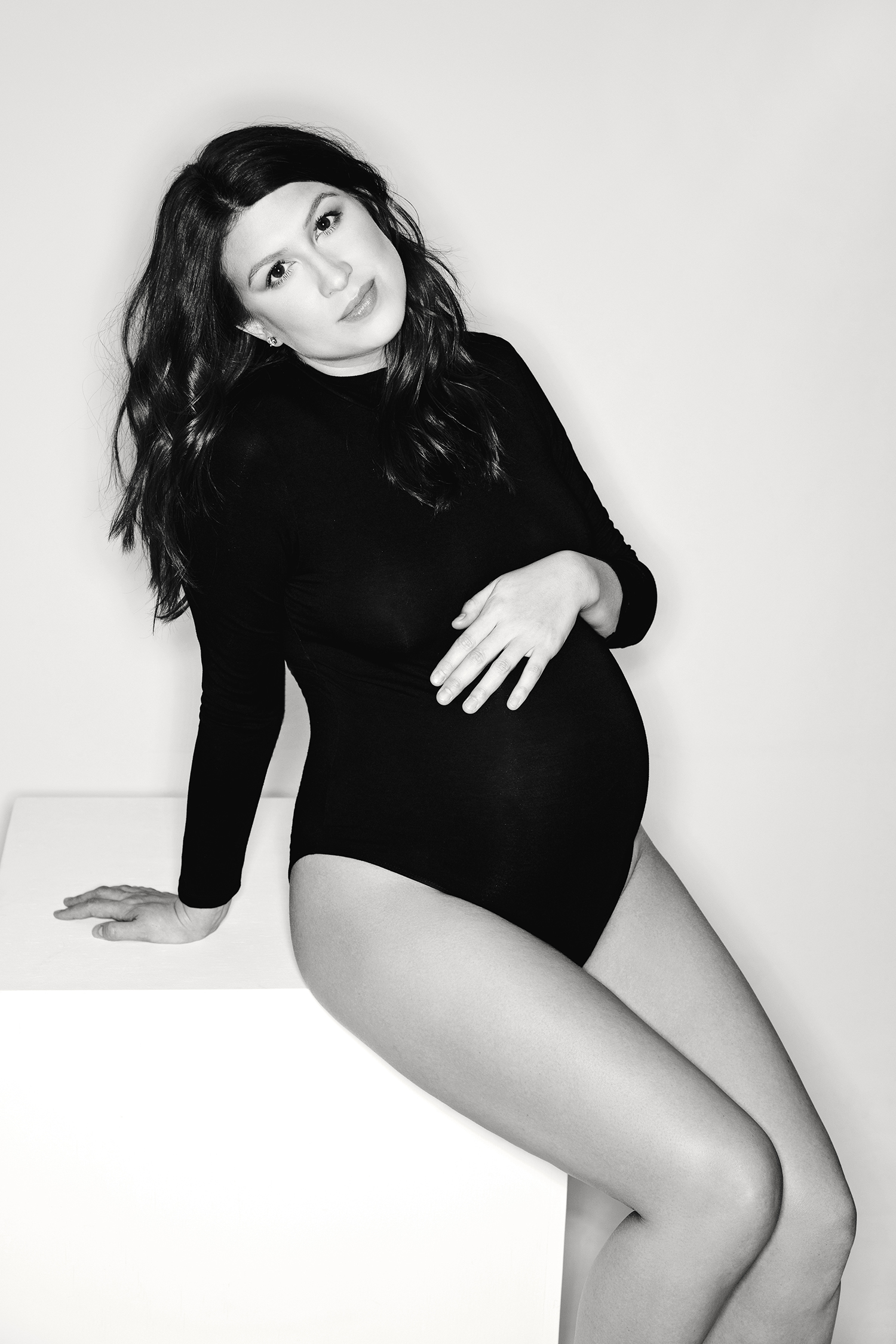 a black and white photo of a pregnant mom in casual clothing sitting down