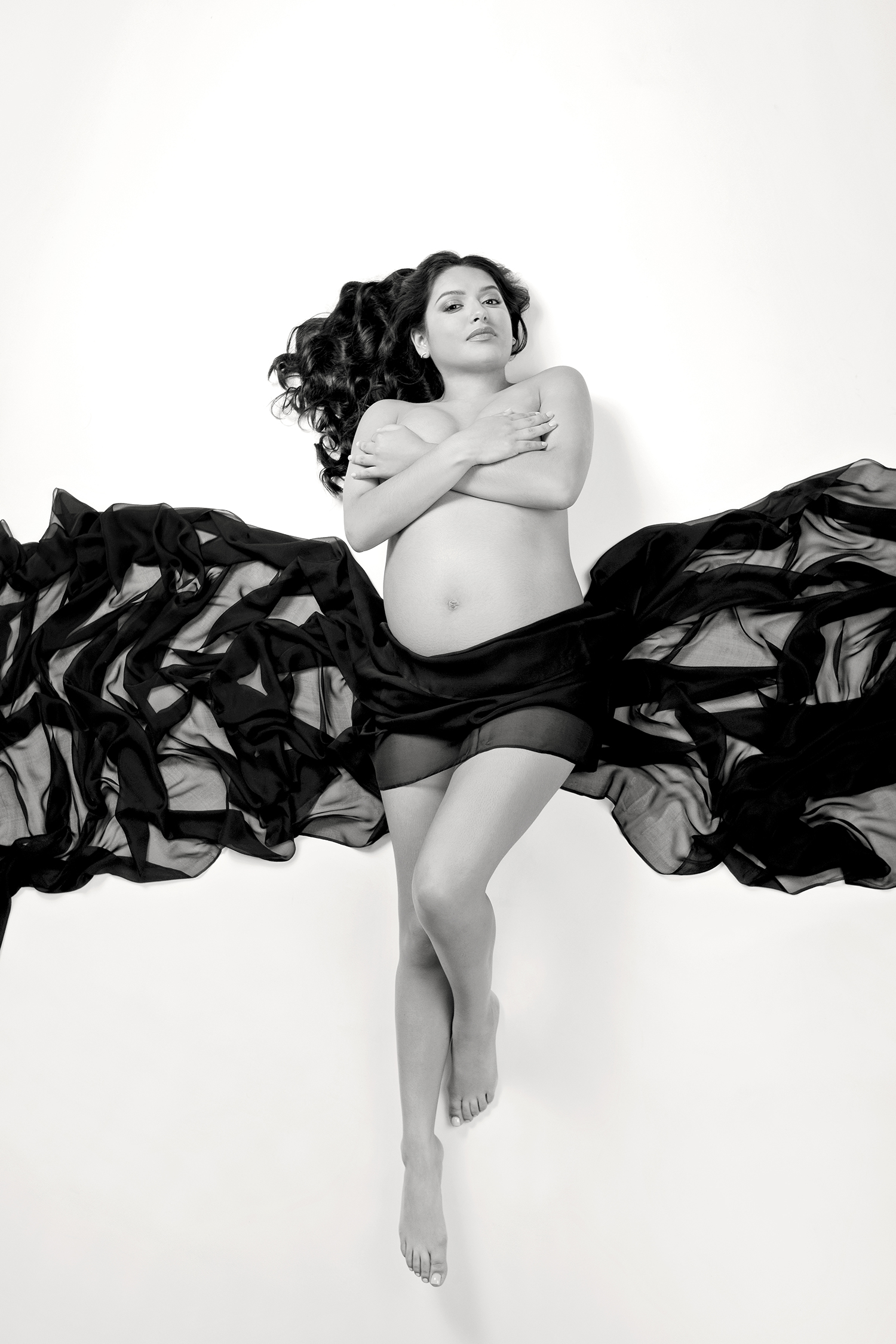 Expectant mother draped in flowing silk fabric in a black and white photo