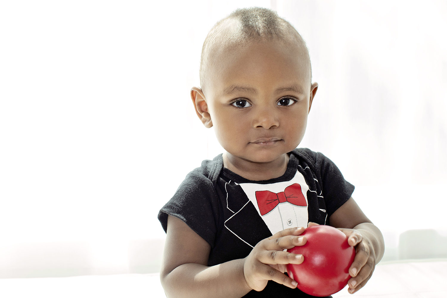 a baby dressed like a little gentleman and holding a red ball