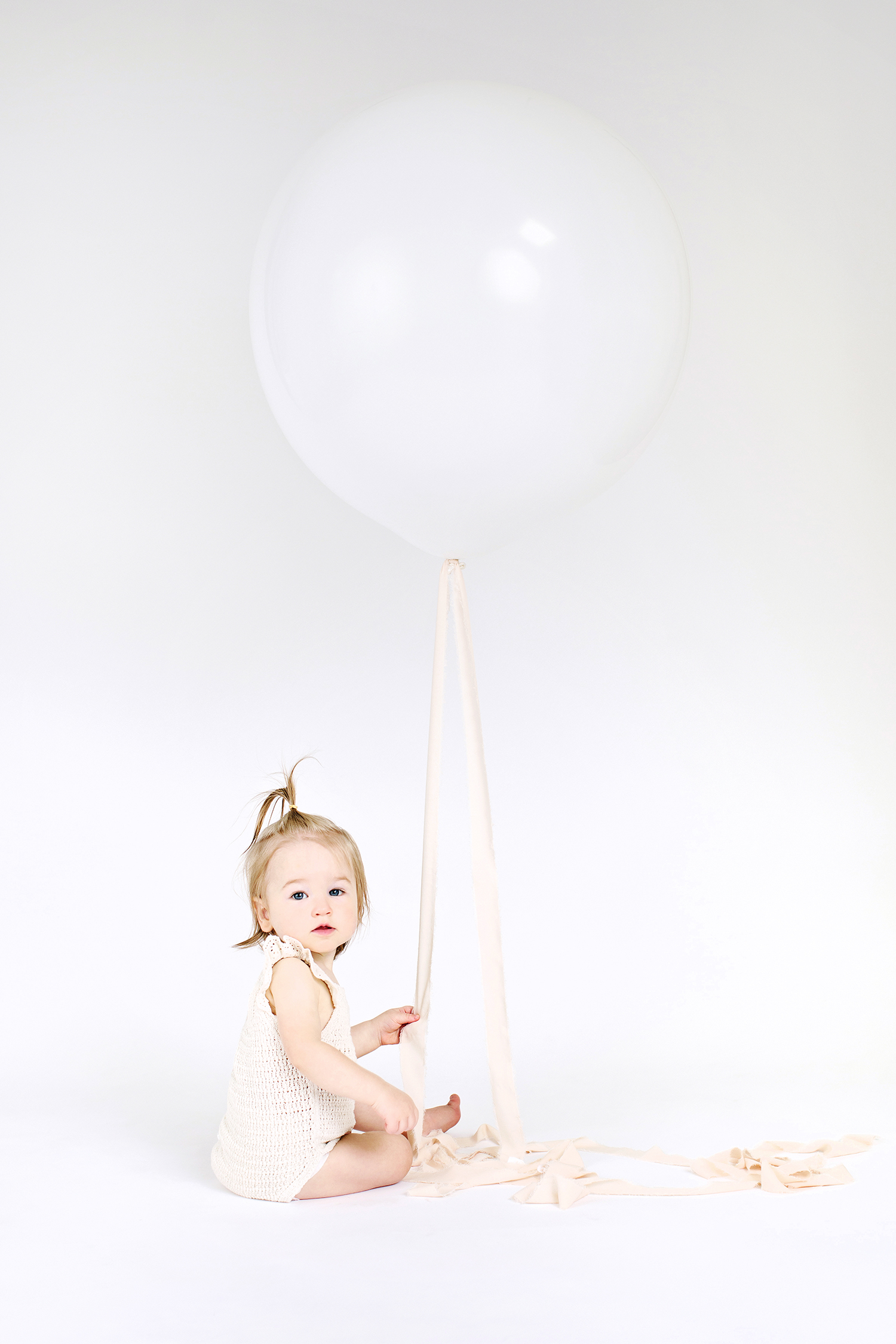 a baby girl holding a single white balloon