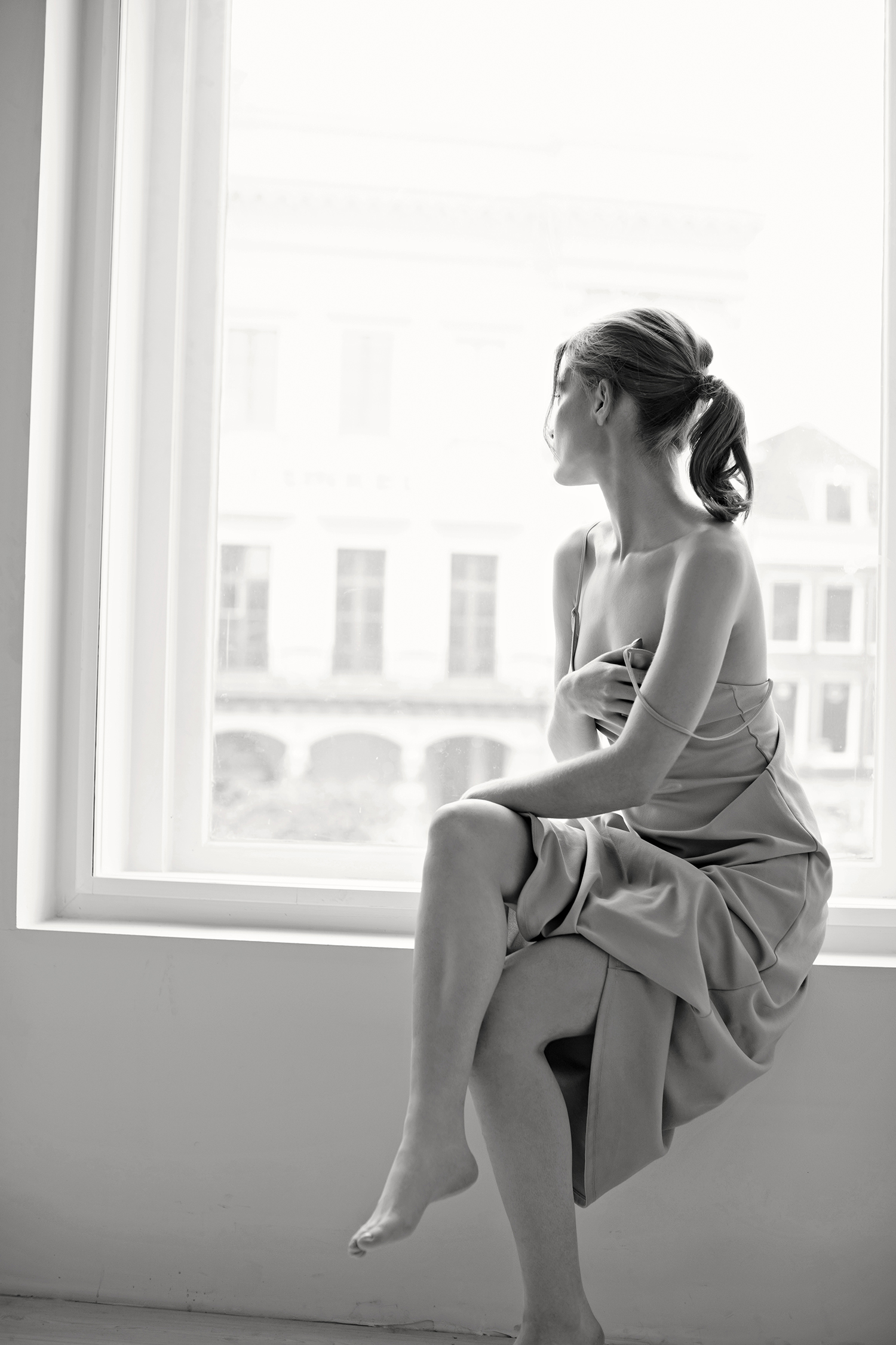 Woman sits by window in editorial boudoir image